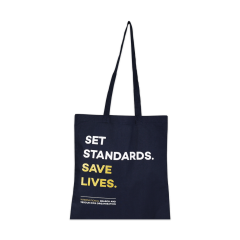 Blaue Stofftasche hängend mit Slogan in Großbuchstaben "Set Standards. Save Lives"